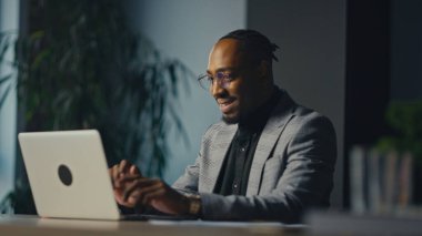 Ofiste dizüstü bilgisayarda çalışan gülümseyen girişimci ya da yönetici, çevrimiçi iletişimle meşgul. Dijital iş akışı, liderlik, modern iş, güven ve profesyonel başarı kavramı