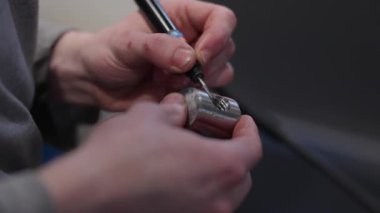 Bir atölyedeki bir metal parçasının iç ipliklerini temizlemek veya cilalamak için el bilgisayarı kullanan bir zanaatkârın yakın çekimi. Hassasiyet, işçilik ve el işi kavramı.