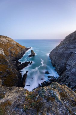 Hafif dalgaların ve alacakaranlıkta sakin bir okyanusun olduğu nefes kesici kayalık bir kıyı şeridini deneyin.