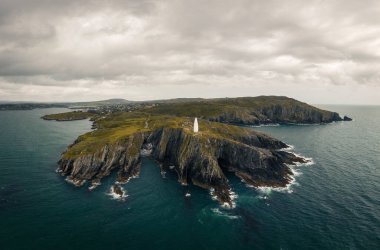 Deniz feneri, engebeli uçurumlar ve kasvetli gökyüzünün altındaki karanlık okyanus sularıyla nefes kesici ada manzarası..