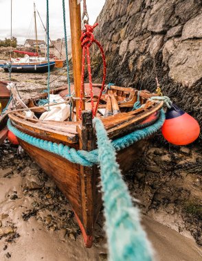 Canlı bir balıkçı teknesi engebeli bir kıyıda demirli, büyüleyici deniz renkleri ve karmaşık dokular sergiliyor.
