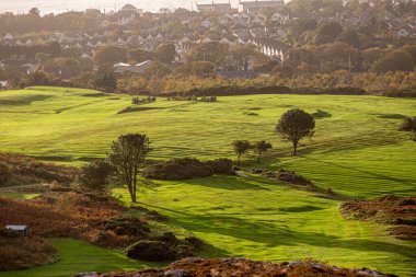 Serin bir gün batımında yemyeşil ve yumuşak ışıklarla güzel bir golf sahasının çarpıcı manzarasını hayal edin.