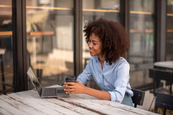 Black woman interested in something on computer screen Computer chatting,  holding cup of coffee in hands socializing with friend
