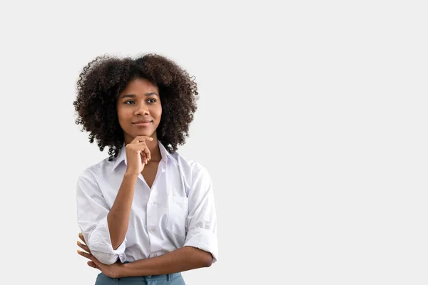 İlginç bir şey düşünen ya da bir şeyler düşünen Afrikalı Amerikalı bir kadının portresi. Beyaz arka planda dururken çenesini tutuyor..