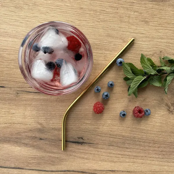 Berries cold drink in a glass with a gold straw