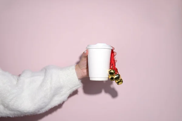 A paper cup in the hands of a woman with Christmas bells. Christmas. New Year