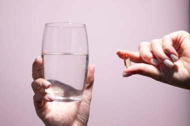 Elimde haplar ve bir bardak su beyaz arka planda izole edilmiş.