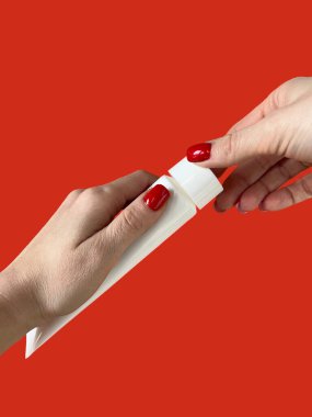 Bir kadın kırmızı arka planda diş macunlu bir tüp tutuyor. Diş bakımı