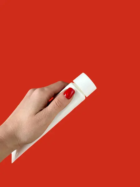 A woman is holding a tube with toothpaste on a red background. Dental care