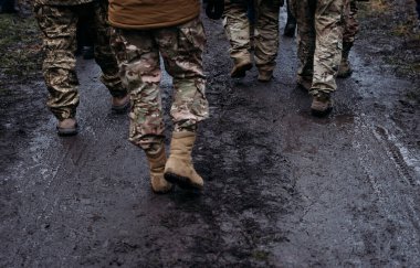 Askeri üniformalı adamlar yağmurdan sonra yolda yürürler. Askerler evlerine dönüyor. Dramatik arka plan, soğuk renkler. Savaş ve barış kavramı, Ukrayna ve Rusya arasındaki çatışma.