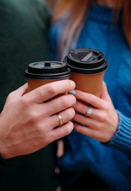 Kapalı çekimde iki tek kullanımlık kahve bardağını tutarken, kadın ve erkek elleri dışarıda bardakları tokuştururken. Sol fincana odaklan.