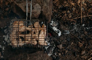 Kuru yaprak ve taşlardan oluşan bir zemin üzerinde üst görünüm: ızgaraların üzerine dizilmiş bir sıra domuz pirzolası, bir sonbahar günü bir ateşin üzerinde kavrulmuş.