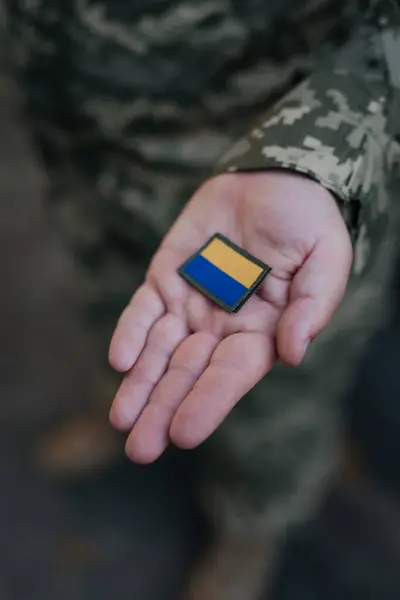 A Ukrainian military man holds the emblem of the national flag in his hand as a symbol of strength. War in Ukraine. Dramatic background, warm colors.