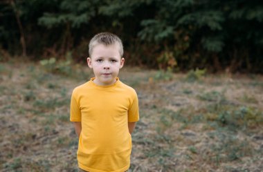 Yazın güzel bir çocuk dışarıda parkta duruyor. Köylü bir çocuk durup kameraya bakıyor. Yatay fotoğraf, sıcak renkler. Reklam mesajınız için bulanık arkaplan ve kopyalama alanı.
