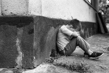 Çocuk hüzünlü bir şekilde yalnız oturuyor. Küçük bir Ukraynalı çocuk elleriyle yüzünü korkuyla kapattı. Aile içi şiddet kavramı. Siyah beyaz fotoğraf.