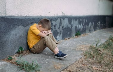 Çocuk hüzünlü bir şekilde yalnız oturuyor. Küçük bir Ukraynalı çocuk elleriyle yüzünü korkuyla kapattı. Reklam mesajınız için bulanık arkaplan ve kopyalama alanı.