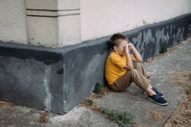 Sarı tişörtlü bir çocuk hüzünlü bir şekilde yalnız oturur. Küçük bir Ukraynalı çocuk elleriyle yüzünü örttü, korkudan ağlıyordu. Aile içi şiddet kavramı..