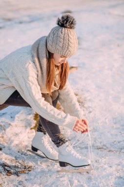 Genç bir kız paten sahasında paten kaymadan önce paten bağlarını bağlıyor. Beyaz bir kazak ve kalın bir şapka giymiş bir kadın bankta oturuyor. Kışın aktif dinlenme.