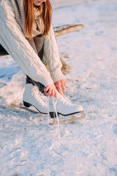 A young girl ties her skate laces before skating at the skating rink. White figure skating skates worn on a woman\'s feet. Side view. Active recreation in winter.