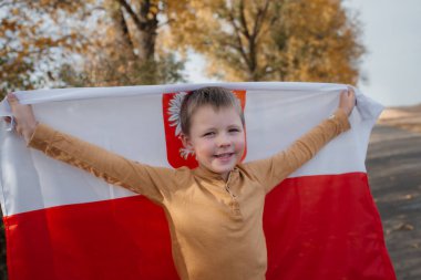 Gülümseyen ve elinde Polonya bayrağını tutan yakışıklı bir çocuk. Ulusal bayrağı olan bir çocuğun portresi. Ulusal bayramlar ve vatanseverlik olayları kavramı. Vatanseverlik.