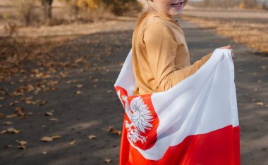 Arkasından küçük bir çocuk elinde Polonya bayrağını tutuyor. Doğada ulusal bayrak taşıyan bir çocuk yolda duruyor. Yakın plan. Tatiller ve vatanseverlik olayları kavramı. Bağımsızlık Günü.