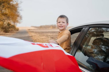 Kahverengi kazaklı küçük bir çocuk gülümsüyor ve elinde Polonya bayrağını tutuyor. Bir çocuk elinde bayrak sallayarak arabadan dışarı bakar. Ulusal bayramlar ve vatanseverlik olayları kavramı. Vatanseverlik.