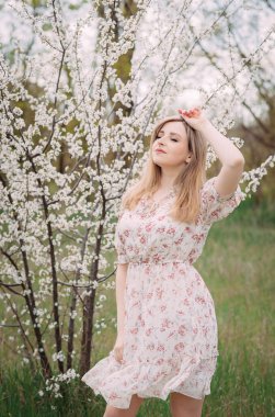 Renkli desenli beyaz elbiseli bir kadın aromayı sever. Bahçedeki çiçek açan bir bahar ağacının yanında güzel genç bir kadın duruyor. Gençlik, aşk, moda, romantizm ve yaşam tarzı konsepti