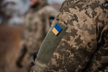 Omzunda ulusal bayrak olan askeri üniformalı Ukraynalı asker. Dramatik arka plan, soğuk renkler. Savaş ve barış kavramı, Ukrayna ve Rusya arasındaki çatışma.