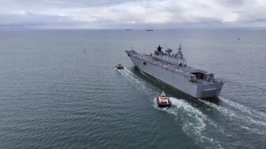 Melbourne, VIC, Avustralya - 23. Mar 2024 - HMAS Adelaide bulutlu bir sabah römorkör eşliğinde Melbourne Limanı 'ndan ayrılıyor.