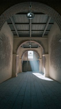 Üç boyutlu, kemerli tuğla duvarlı, geniş pencereli ve ahşap merdivenli eski bir oda. Atmosferik ışık çarpıcı bir endüstriyel klasik mimari iç mekan yaratıyor..