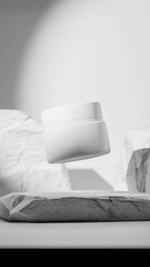 Doğal taşlar arasında süzülen beyaz kozmetik bir kavanozun zarif üç boyutlu görüntüsü. Cilt bakımı, güzellik markalaşması veya lüks kozmetik sunumları için minimal ürün modelleme tasarımı.
