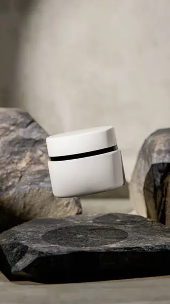 Doğal taşlar arasında süzülen beyaz kozmetik bir kavanozun zarif üç boyutlu görüntüsü. Cilt bakımı, güzellik markalaşması veya lüks kozmetik sunumları için minimal ürün modelleme tasarımı.