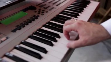 Elektronik piyano çalan bir müzisyenin elleri, bir sentezleyici. Sesleri karıştırıyor. Caz, rock, pop müzik. Müzisyenlerin elleri bir sentezleyicinin anahtarında, arka planda, tonlanmış. Bir erkeğin ellerine yakın.