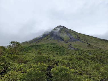 Arenal Volkanı, La Fortuna, Kosta Rika. La Fortuna, Kosta Rika 'daki zirveyi çevreleyen bulutlu Arenal Volkanı. Yeşil yapraklar ve tropikal ormanlar.