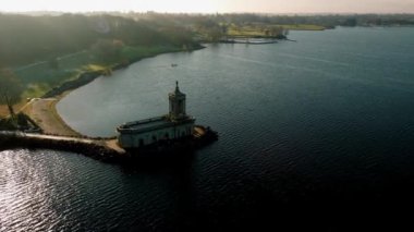 Hava görüntüsü, güneşli bir kış gününde, Rutland Su Gölü rezervuarının küçük bir çıkıntısında Normanton kilise manastırının panoramik paraşütünü 4k aşağı çekti..