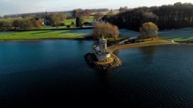 Hava görüntüsü, güneşli bir kış gününde, Rutland Su Gölü rezervuarının küçük bir çıkıntısında Normanton kilise manastırının panoramik paraşütünü 4k aşağı çekti..