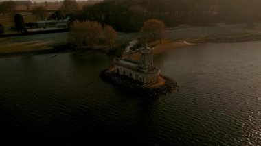 Hava görüntüsü, güneşli bir kış gününde, Rutland Su Gölü rezervuarının küçük bir çıkıntısında Normanton kilise manastırının panoramik paraşütünü 4k aşağı çekti..