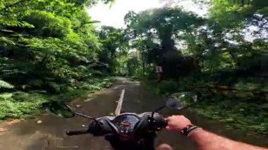 Point of view driving riding a motorbike scooter along tropical roads in the Philippines, Asia. lush green jungle and bright sunshine, travel content, scenic tourism, vacation holiday 