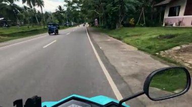 Point of view driving riding a motorbike scooter along tropical roads in the Philippines, Asia. lush green jungle and bright sunshine, travel content, scenic tourism, vacation holiday 