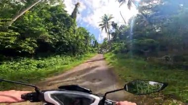 Point of view driving riding a motorbike scooter along tropical roads in the Philippines, Asia. lush green jungle and bright sunshine, travel content, scenic tourism, vacation holiday 