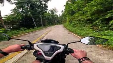 Point of view driving riding a motorbike scooter along tropical roads in the Philippines, Asia. lush green jungle and bright sunshine, travel content, scenic tourism, vacation holiday 