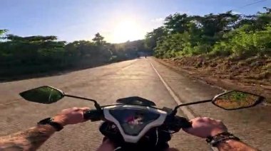Point of view driving riding a motorbike scooter along tropical roads in the Philippines, Asia. lush green jungle and bright sunshine, travel content, scenic tourism, vacation holiday 