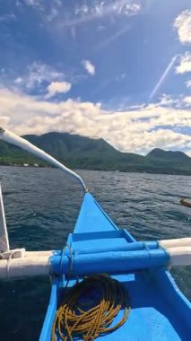 Point of view riding Bangka boat across tropical seas, Camiguin island volcanic mountain range and green landscape, Asia Philippines backpacking, holiday tourism vacation