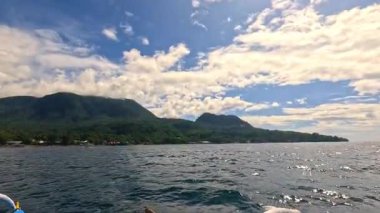 Point of view riding Bangka boat across tropical seas, Camiguin island volcanic mountain range and green landscape, Asia Philippines backpacking, holiday tourism vacation