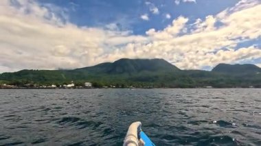 Point of view riding Bangka boat across tropical seas, Camiguin island volcanic mountain range and green landscape, Asia Philippines backpacking, holiday tourism vacation
