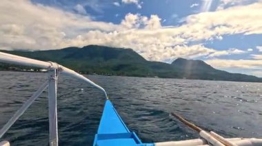 Point of view riding Bangka boat across tropical seas, Camiguin island volcanic mountain range and green landscape, Asia Philippines backpacking, holiday tourism vacation