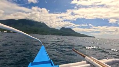 Point of view riding Bangka boat across tropical seas, Camiguin island volcanic mountain range and green landscape, Asia Philippines backpacking, holiday tourism vacation