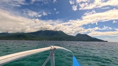 Point of view riding Bangka boat across tropical seas, Camiguin island volcanic mountain range and green landscape, Asia Philippines backpacking, holiday tourism vacation