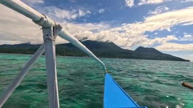 Point of view riding Bangka boat across tropical seas, Camiguin island volcanic mountain range and green landscape, Asia Philippines backpacking, holiday tourism vacation