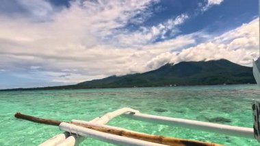 Point of view riding Bangka boat across tropical seas, Camiguin island volcanic mountain range and green landscape, Asia Philippines backpacking, holiday tourism vacation